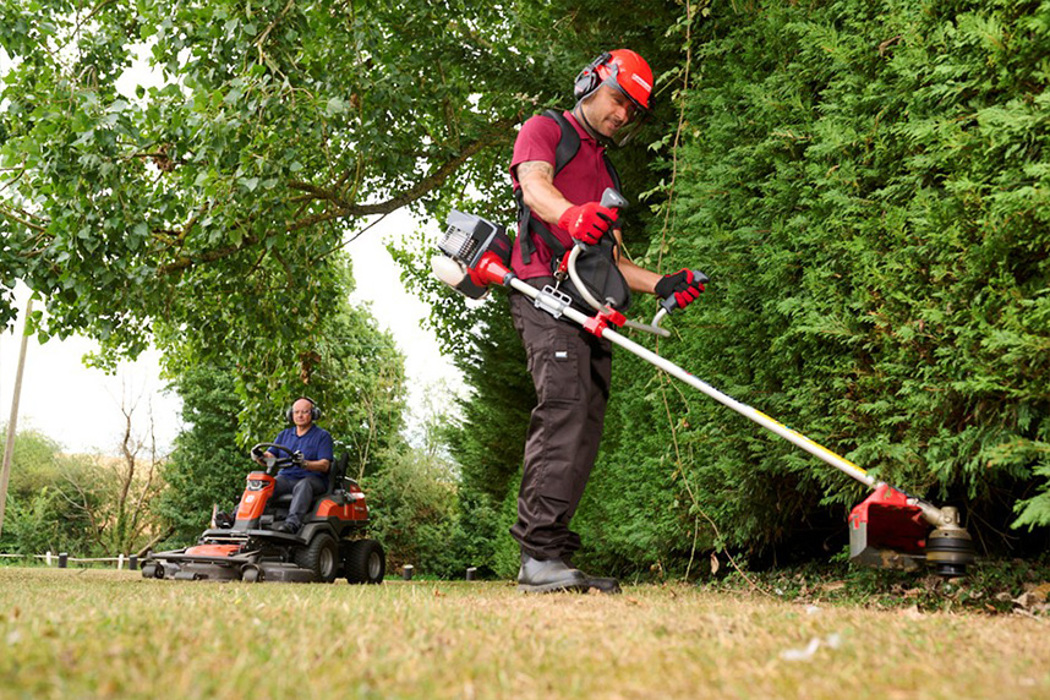 Landscaper using a professional Kawasaki powered brushcutter while another landscaper mows with a Kawasaki powered mower